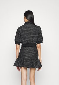 Svart texturerad tvättsats med en kort jacka med korta ärmar och en volangkantad kjol, båda med metalliska detaljer och elastiska manschetter.