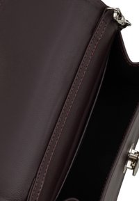 Borsa a borsa in pelle bordeaux con una texture liscia, caratterizzata da cuciture a contrasto e una chiusura in argento, parzialmente aperta per rivelare un interno scuro.