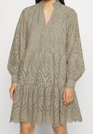 Jasnooliwkowa sukienka z wysokim kołnierzem, długimi balonowymi rękawami oraz misternymi wzorami wycięć ażurowych, z falbanianym dołem i falistym brzegiem.