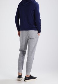 Námořnická mikina s kapucí na šňůrku, spárovaná se šedými joggingovými kalhotami. Kalhoty mají zúžený střih a elastické manžety. Černé tenisky dokončují outfit.