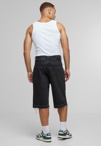 Svarte denimshorts med slitt kant, fem-lommer design og beltehemper. Sammen med en hvit tanktop og grønne/hvite joggesko.
