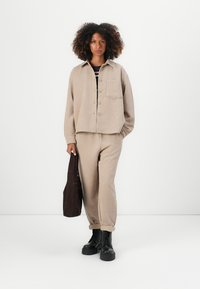 Giacca in corduroy beige con bottoni, abbinata a pantaloni coordinati. Stivali neri alla caviglia e una borsa marrone completano l'outfit.