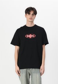 Svart bomull t-skjorte med rund hals og korte ermer. Har et sentralt logo i rosa og rødt i en oval form.