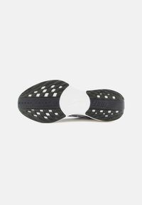 Suela de zapatilla deportiva en blanco y negro, con un patrón de rejilla, goma texturada para tracción, y con una marca en la parte trasera y en el mediopié.