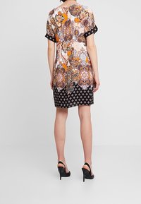 Vestido de manga corta con un colorido patrón de cachemira en tonos naranjas y blancos, parte inferior geométrica negra y textura de tela suave.