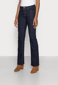 Dark blue denim jeans with a straight leg design, featuring orange stitching and front pockets. Worn with brown heeled boots.