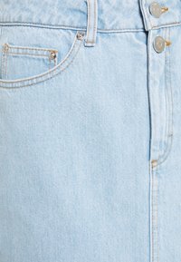 Gonna di jeans azzurri chiari con due bottoni metallici in vita, dotata di una tasca frontale e dettagli di cucitura visibili lungo le cuciture.