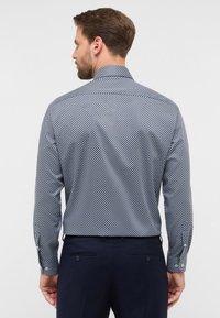 Camicia a maniche lunghe di colore blu navy con un motivo a rombi, realizzata in tessuto morbido. Presenta un colletto standard e polsini con bottoni, indossata con pantaloni scuri.