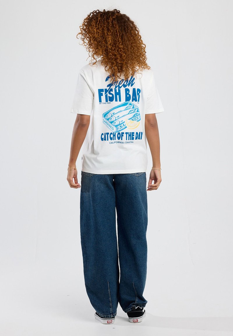 White t-shirt with blue graphic design featuring fish and text "Fresh Fish Bar." Paired with wide-leg blue jeans and black shoes.