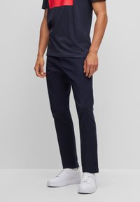 Navy blue cotton chinos with a slim fit, featuring front pockets and a smooth texture. Paired with white sneakers and a dark t-shirt.