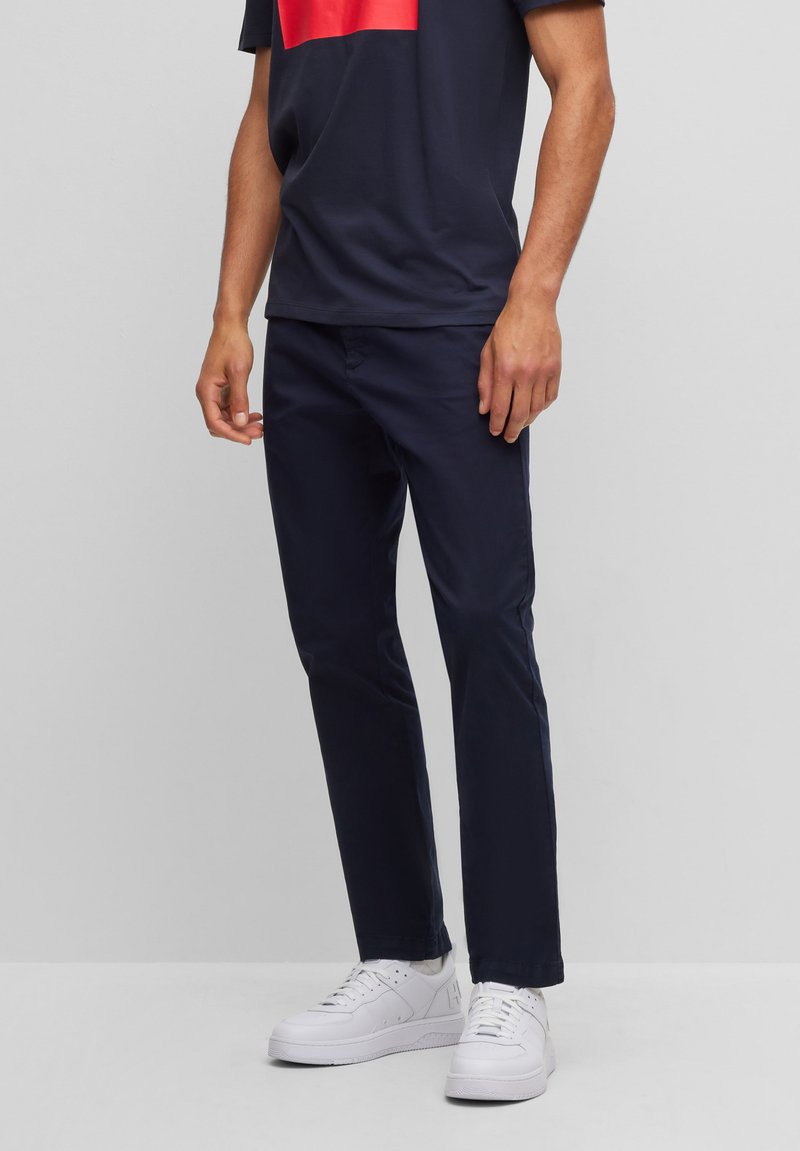 Navy blue cotton chinos with a slim fit, featuring front pockets and a smooth texture. Paired with white sneakers and a dark t-shirt.