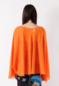 Top arancione in chiffon, comodo e di taglio largo, con scollatura ampia e maniche fluide, caratterizzato da una texture liscia e una qualità trasparente. Etichetta visibile sul retro.