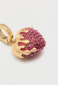 Χρυσή αγκράφα με γοητευτικό στοιχείο σε σχήμα καρδιάς που διαθέτει ροζ στρας και χρυστό σχέδιο σταγόνας σε απλό λευκό φόντο.