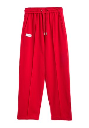 Pantalones casuales de color rojo brillante con cintura elástica, cordón, bolsillos laterales y una pequeña etiqueta rectangular blanca en el muslo izquierdo.