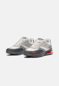 Zapatillas deportivas grises y blancas con paneles de malla, punta redondeada, diseño con cordones y una amortiguación de aire naranja en la suela. Logo de Kappa visible.