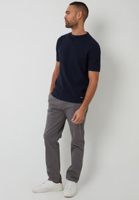 Camisa de punto azul marino de manga corta con patrón texturizado, combinada con pantalones gris claro y zapatillas blancas. Ajuste casual con cuello redondo.