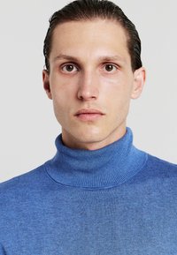 Blauer Rollkragenpullover aus weichem Stoff, mit einem gerippten Halsauschnitt und glatter Textur, der eng am Hals und Oberkörper anliegt.