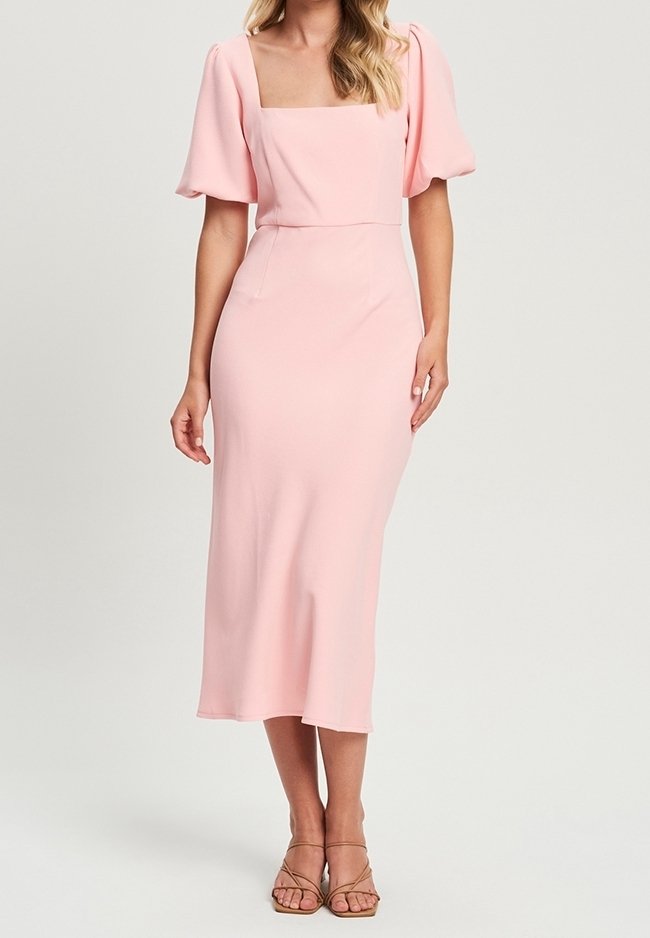 Robe midi à manches bouffantes et encolure carrée, de couleur rose clair, confectionnée dans un tissu lisse avec une taille cintrée et un bas légèrement évasé. Sandales à lanières.