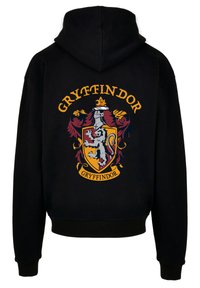 Sort hættejakke med Gryffindor-våbenskjold, der viser en løve, en ridder og gyldne detaljer. Klassisk pasform med kangaroo-lomme og ribbede manchetter.