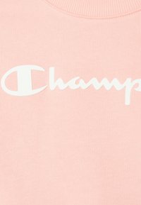 Felpa rosa chiaro con un grande logo bianco "Champion" sul davanti, realizzata in un tessuto morbido e con un collo a costine.