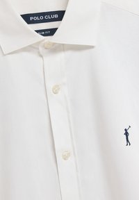 Camicia bianca slim-fit con chiusura a bottoni, caratterizzata da un logo di un golfista ricamato in blu navy sul lato sinistro. Tessuto liscio e leggero.