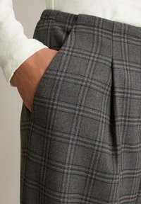 Grijze geruite broeken met een geweven textuur, voorzien van een subtiel ruitpatroon en gele accentstiksel. Inclusief zijzakken en plooien.