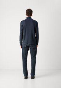 Polo shirt a maniche lunghe color navy con colletto, texture liscia e orlo posteriore leggermente più lungo, abbinato a pantaloni in denim scuro.