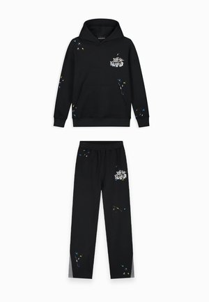 Zwart hoodie en sweatpants set met kleurrijke verfspetterdetails en witte "Black Bananas" tekstlogo op de voorkant.