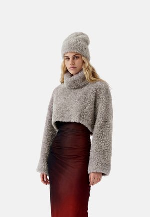 Donna con maglione corto grigio peloso e cappello abbinato con gonna aderente a vita alta rosso scuro su sfondo bianco.