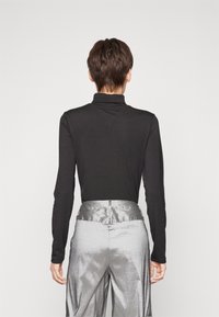 Svart långärmad topp med hög krage, kombinerad med blanka silvriga byxor med en strukturerad midja och avslappnad passform.