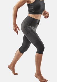 Schwarzes sportliches Crop-Top und knielange Leggings, die ein figurbetontes Design, strukturierten Stoff und dezente Panelelemente aufweisen.