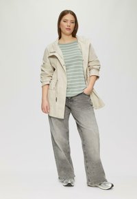 Veste zippée beige clair avec taille réglable, chemise rayée vert menthe, jeans à jambes larges gris et chaussures de sport argentées. Textures de tissu lisses.