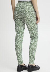 Groene broek met patroon en een witte abstracte print, elastische tailleband en slim fit, gecombineerd met zwarte schoenen.