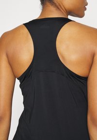 Top sportivo nero senza maniche con design a schiena scoperta, realizzato in tessuto traspirante con una texture liscia e una minimalista etichetta sul retro.
