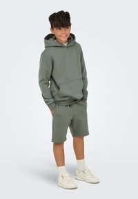 Grøn bomulds hoodie med frontlomme, parret med matchende shorts. Høje hvide sneakers og ribbede crew-sokker fuldender outfittet.