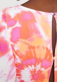 Gros plan sur une robe à fermeture au dos avec un motif tie-dye rose, orange et blanc, et un bouton argenté au niveau de l'encolure.