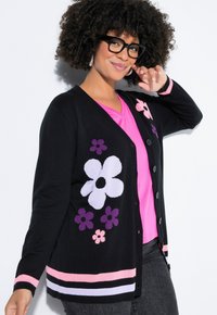 Schwarzer Cardigan mit bunten Blumenmustern, ausgestattet mit einer Knopfleiste, langen Ärmeln und pink gestreiften Akzenten am Saum und an den Bündchen.