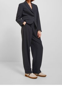 Tmavý elegantní blazer s jedním knoflíkem, doplněný širokými kalhotami. Oblečen�í je doplněno světlými, texturovanými teniskami.