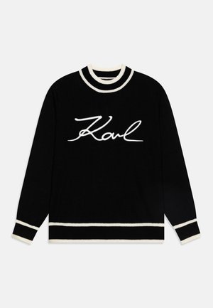 Un pull noir avec un logo en écriture blanche "Karl" au centre, et des détails en côtes rayées blanches et noires au col et aux poignets.