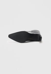 Μαύρο μποτάκι με τακούνι, μυτερή μύτη και υφή στην επιφάνεια, με παχιά σόλα και κομψό σχεδιασμό. Λείο φινίρισμα με λεπτομέρειες ραβδώσεων στη σόλα.