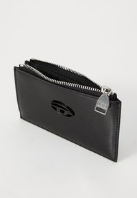 Cartera de cuero negro con superficie texturizada, cierre de cremallera, herrajes plateados y acento de logo circular. Diseño rectangular compacto.