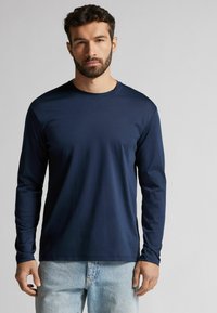 Maglietta a maniche lunghe navy con colletto a girocollo, realizzata in tessuto liscio. Presenta maniche aderenti e un orlo dritto, abbinata a jeans azzurri.