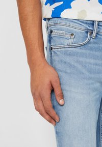 Lichtblauwe denim jeans met een slim fit, voorzien van contrasterende stiksels, metalen klinknagels en een leren label op de achterzak.