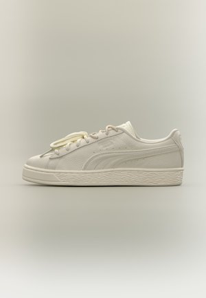 Άσπρο δερμάτινο sneaker χαμηλού τύπου με υφή στη σόλα, λεπτομέρεια πλευρικής ρίγας και άσπρα κορδόνια πάνω σε ουδέτερο φόντο.