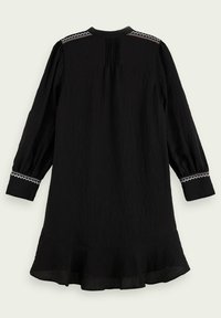 Černé šaty s dlouhým rukávem, vyrobené z texturované látky, s nařaseným zadním dílem a vy�šívanými akcenty na ramenou a manžetách. Podrážení se širokým lemem.