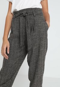Pantalon en noir et blanc à motif en chevrons avec taille à cordon, poches latérales et coupe décontractée, fabriqué à partir d'un tissu texturé.