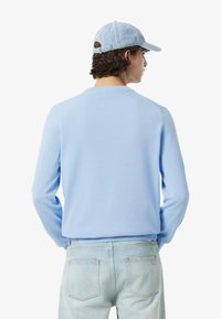 Lichtblauwe trui met een ronde hals, lange mouwen en geribbelde manchetten, gecombineerd met lichtdenim jeans en een lichtblauwe pet.