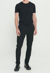 Zwart t-shirt met een ronde hals en korte mouwen, gecombineerd met zwarte joggingsbroek met een verstelbare trekkoord tailleband. Zwarte sneakers.