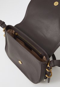 Καφέ δερμάτινη τσάντα χιαστί με χρυσές λεπτομέρειες, που διαθέτει εσωτερική τσέπη με φερμουάρ και λεία υφή. Κλείσιμο με μαγνητικό κούμπωμα.