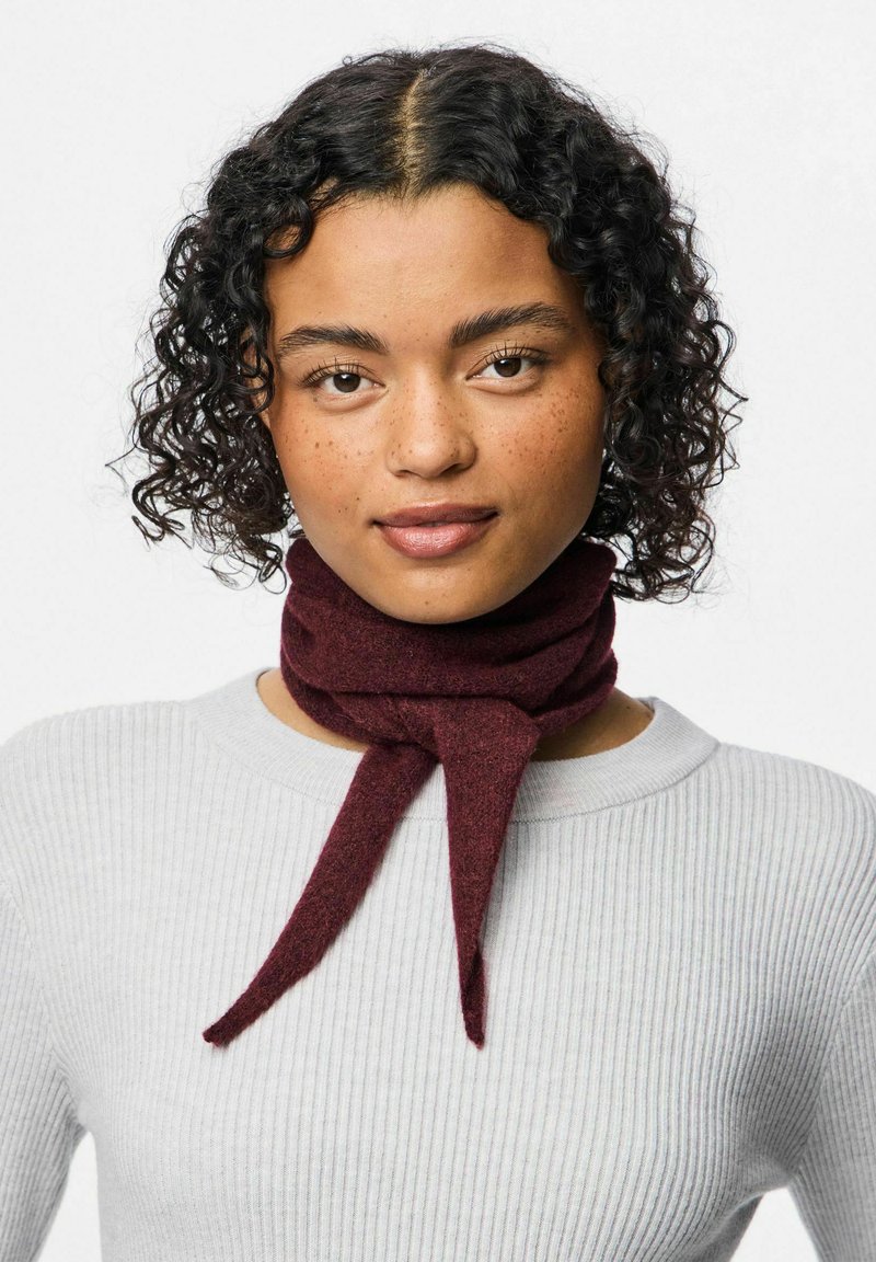 Bordo vilnonis šalikas, surištas mazgu, dėvimas ant šviesiai pilkos nertinės megztos palaidinės. Lygus paviršius, vidutinio pločio ir pailgos formos.